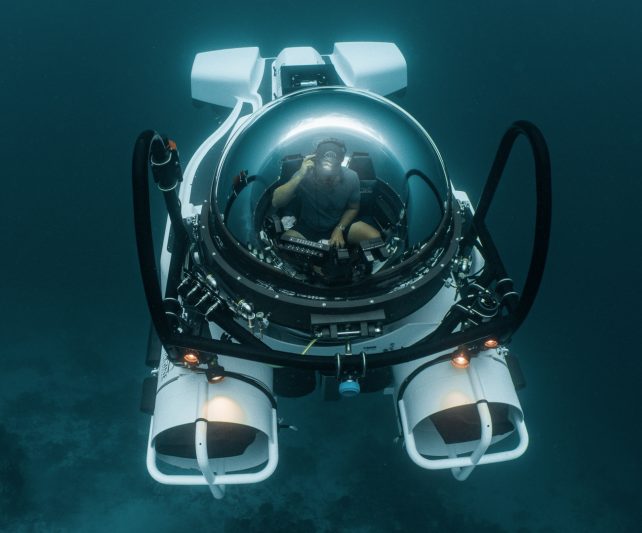 underwater view from above of a pilot inside a submersible in the ocean in the maldives