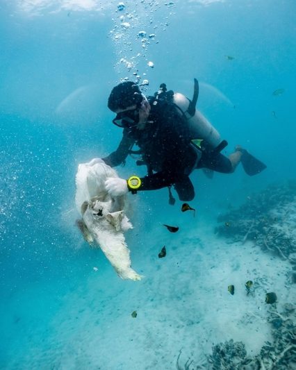 diver underwater in the maldives holding a bag and some debris during a reef clean up