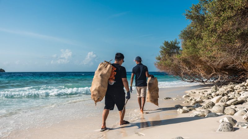 two people walking on a beach in the maldives carrying bags during a beach clean up