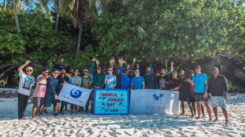 a group of people on a beach in the maldives holding signs and banners after a beach clean up for world ocean day