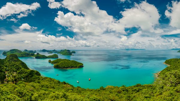 aerial view of a calm tropical turquoise lagoon with green jungle mountains and coastline, a few boats near the shore