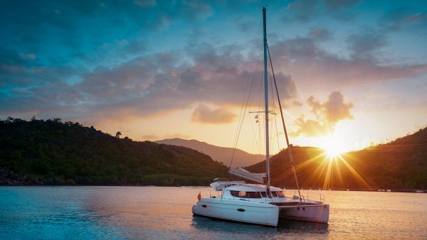 a white catamaran in front of islands with the sun setting
