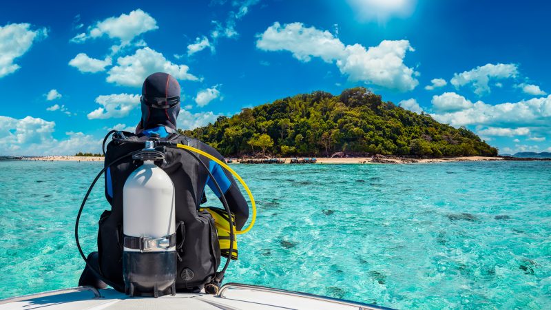 A scuba diver sits on a boat and looks at the turquoise sea